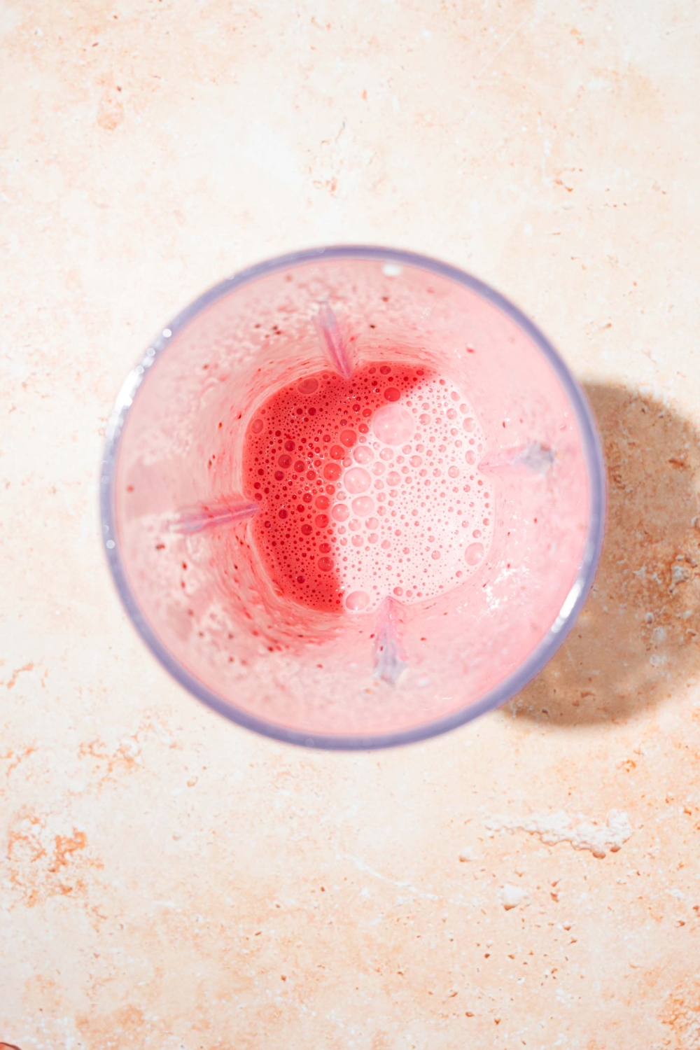 A blender mixing strawberries and yogurt to make dip. The blender is on a tan counter.