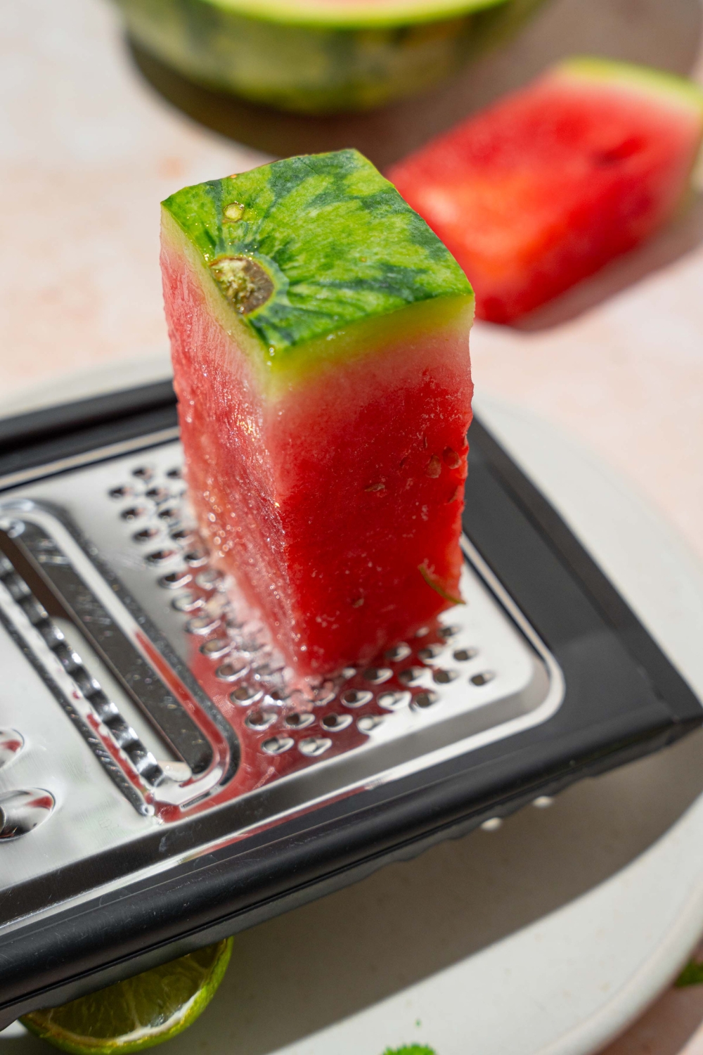A frozen watermelon wedge on a food grater. The grater is over a white plate.