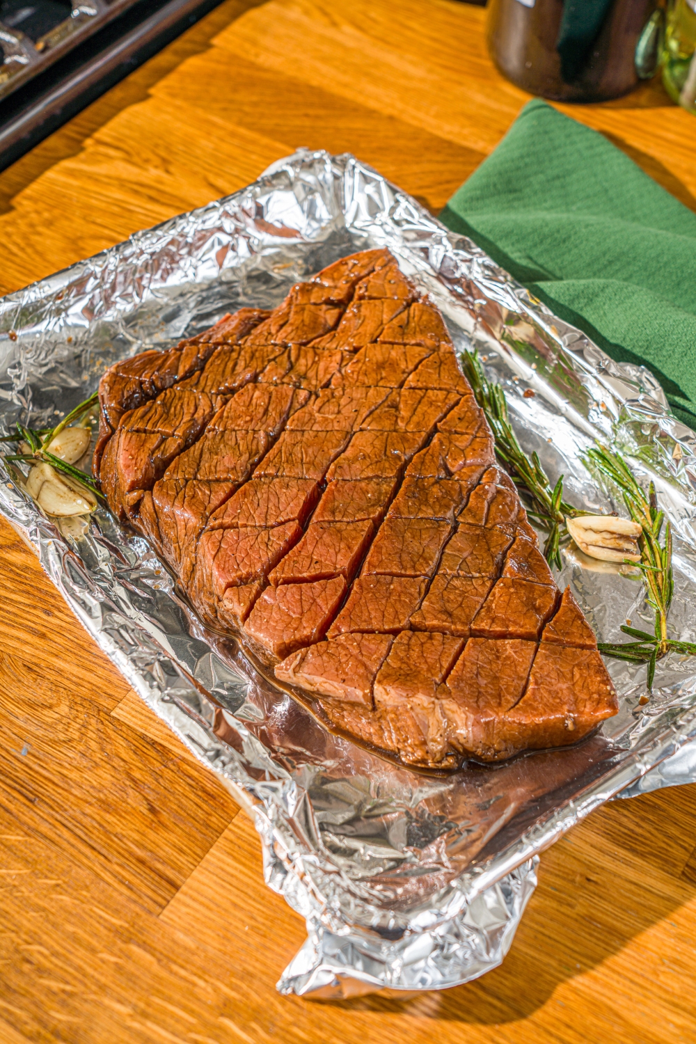 A baking sheet lined with foil with marinated London broil beef with garlic and rosemary. The sheet is on a wooden counter.