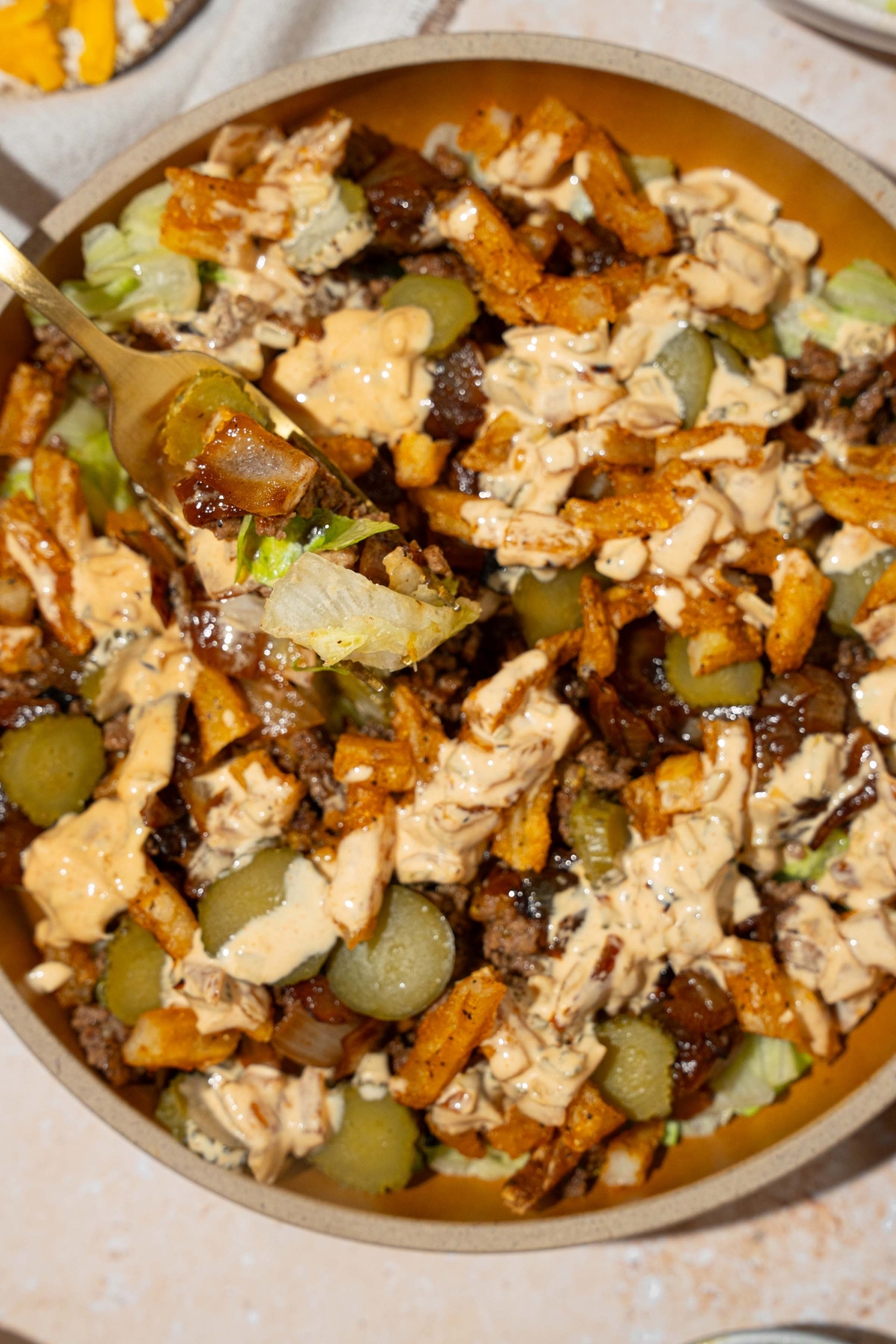 An orange bowl with an In-n-Out burger bowl with shredded lettuce, seasoned burger meat, french fries, pickles, and In-n-Out sauce. A fork is in the plate. The plate is on a tan counter.