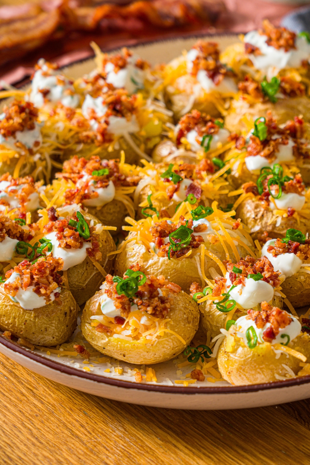 A white plate with mini baked potatoes loaded with sour cream, shredded cheese, and crumbled bacon, garnished with sliced green onion.