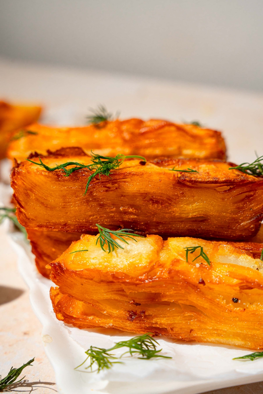 A loaf pan lined with parchment paper with thinly sliced potatoes soaked in cream and layered in the pan. The pan is on a tan counter.