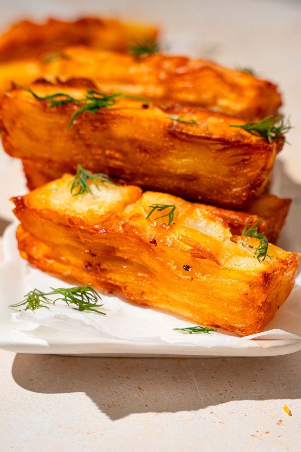 A loaf pan lined with parchment paper with thinly sliced potatoes soaked in cream and layered in the pan. The pan is on a tan counter.
