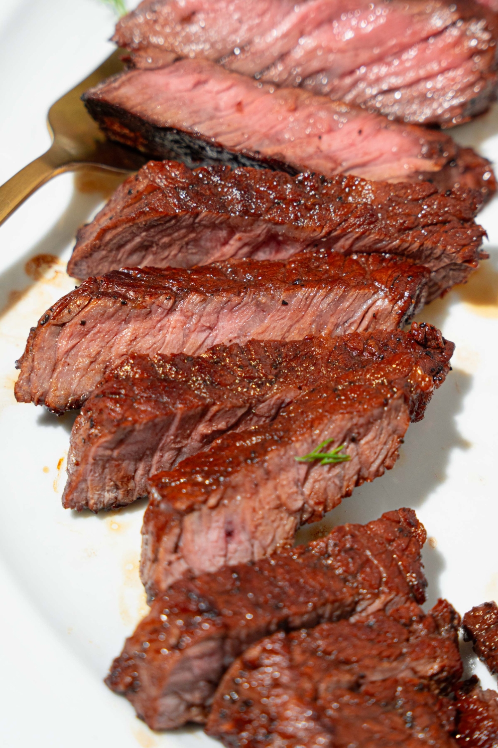 A white plate with sliced marinated skirt steak. There is a fork on the plate.
