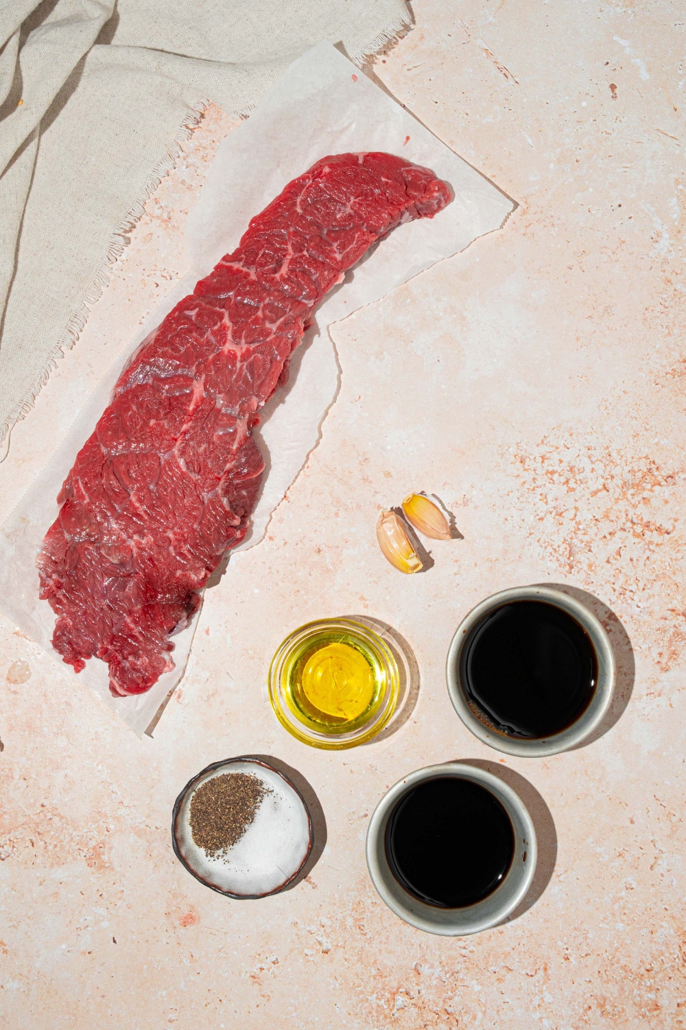 A tan counter with ingredients to make skirt steak marinade including skirt steak, soy sauce, balsamic vinegar, olive oil, garlic, salt, and pepper.