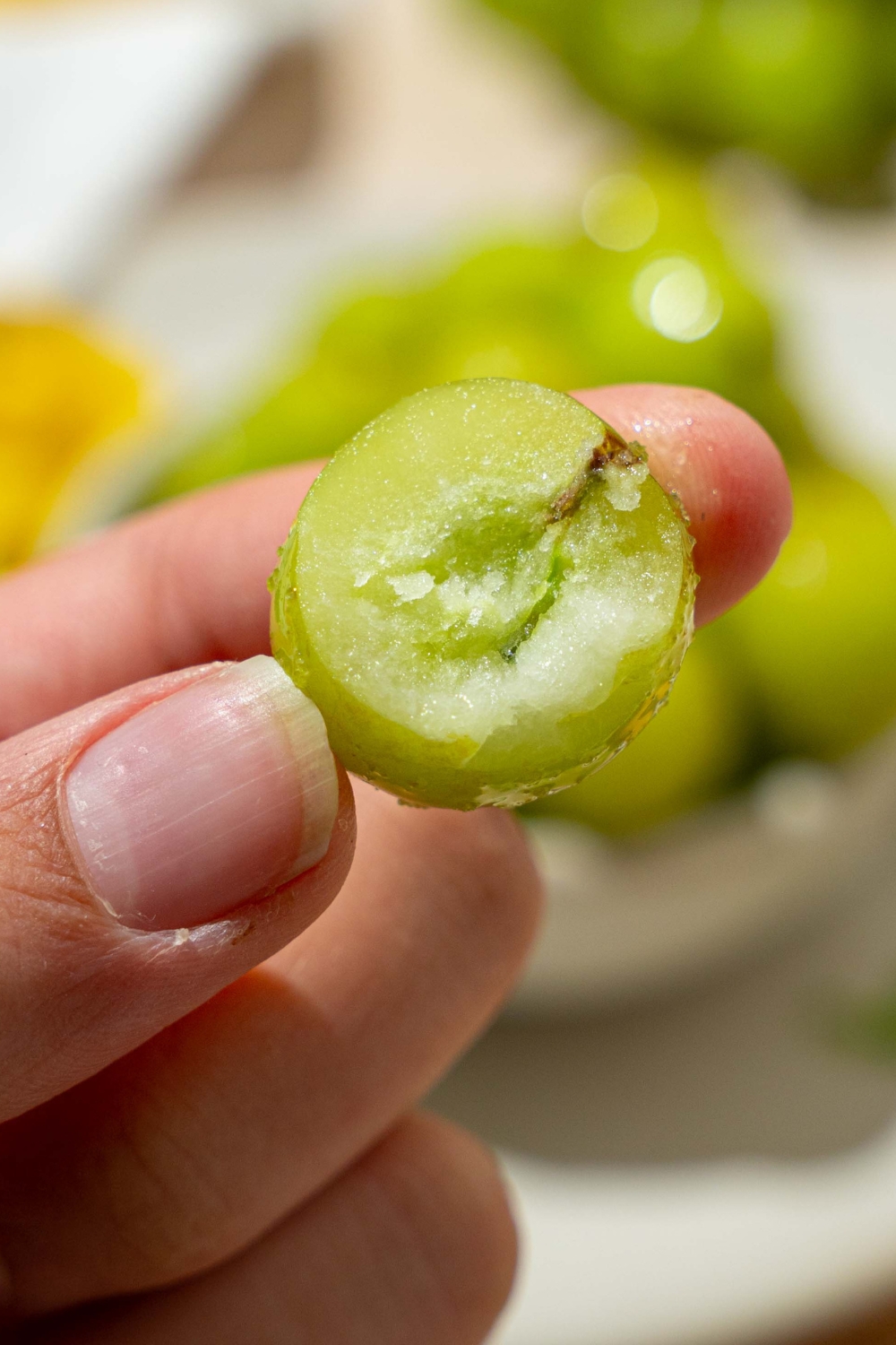 A hand holding a green frozen sour grape that has a bite taken out of it.