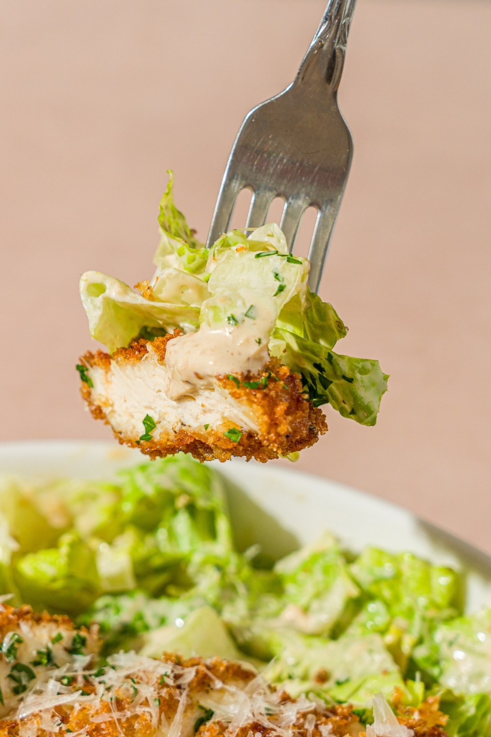 A fork with a bite of crispy chicken caesar salad over a bowl of caesar salad.