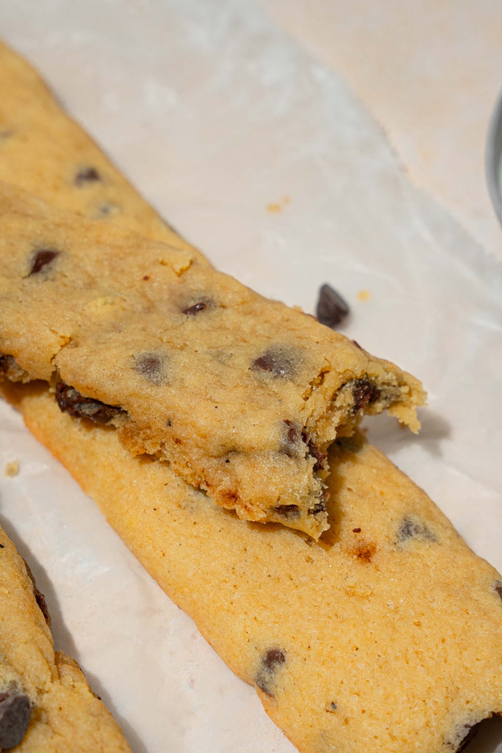 A piece of parchment paper with chocolate chip cookie fries. One of the cookies has a bite taken from it.