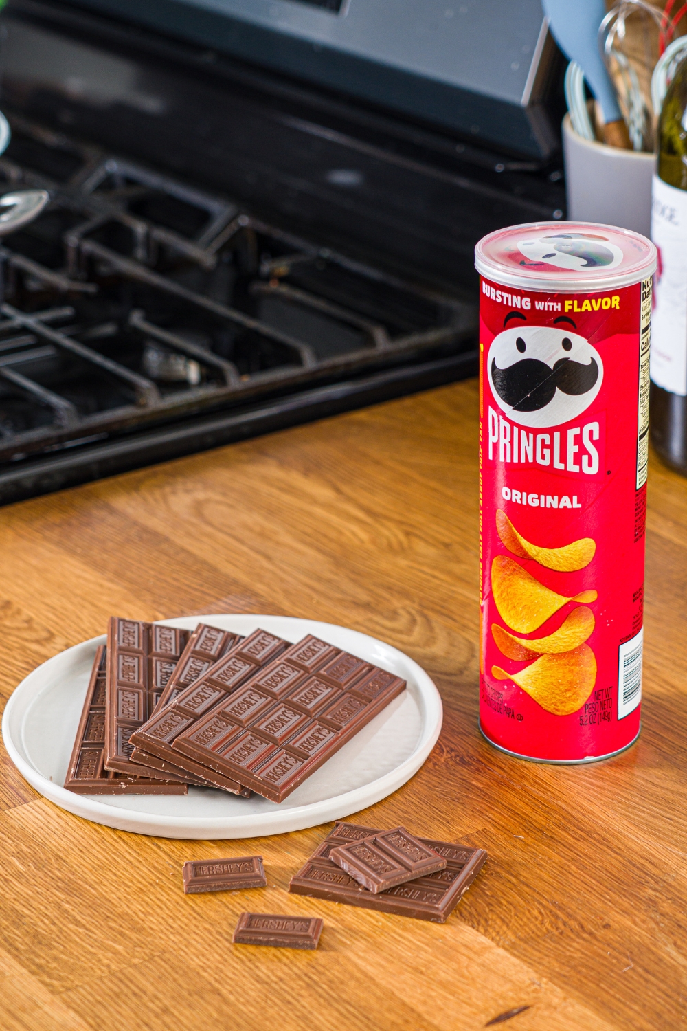 A can of Pringles and a white plate with Hershey's chocolate bars on it. Both are on a wooden counter.