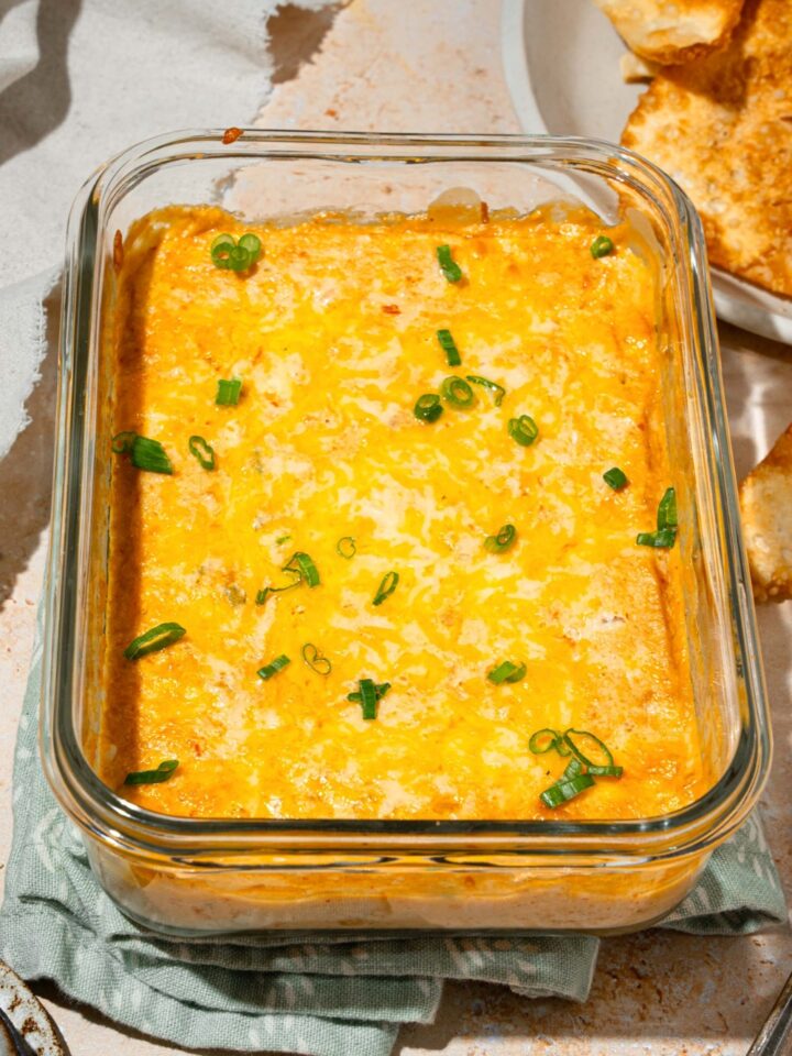 Crab rangoon dip in a glass baking dish with a plate of wonton chips in front of it off to the right.