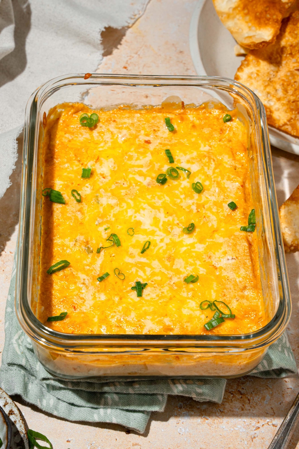 Crab rangoon dip in a glass baking dish with a plate of wonton chips in front of it off to the right.