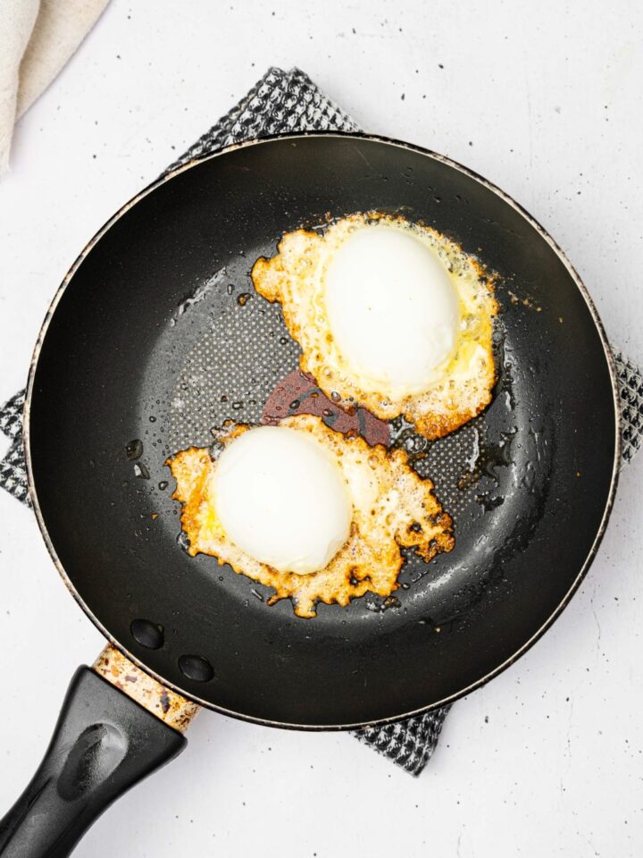 Two jammy eggs on top of crispy feta in a black skillet.