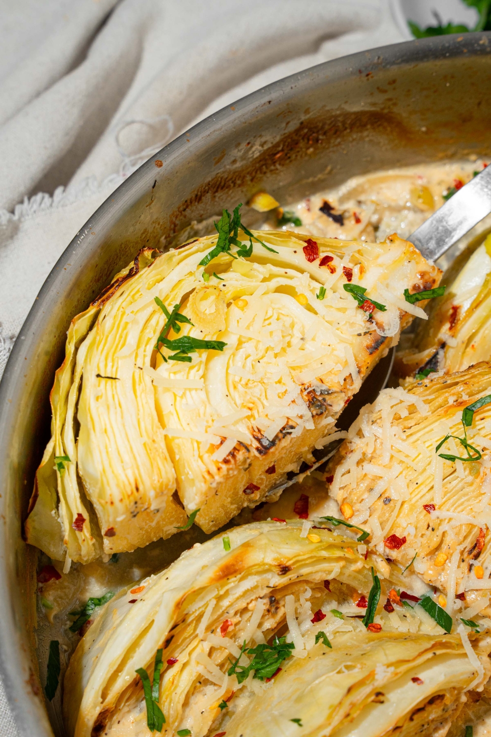 A skillet with baked garlic parmesan melting cabbage garnished with fresh parsley, red pepper flakes, and shredded parmesan cheese.