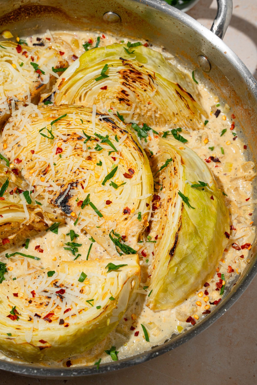 A skillet with baked garlic parmesan melting cabbage garnished with fresh parsley, red pepper flakes, and shredded parmesan cheese.