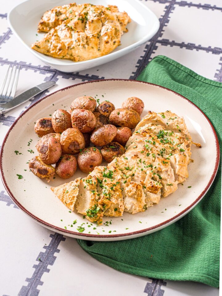 Greek yogurt marinated chicken breast sliced on a white plate with baby potatoes.