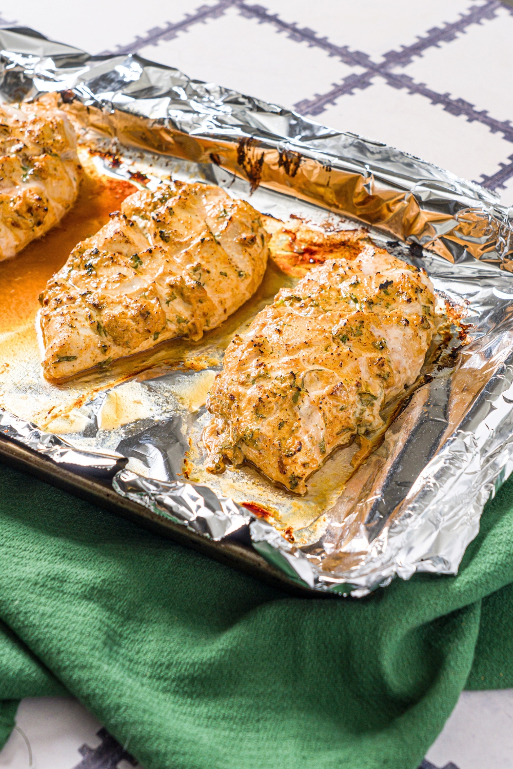 Two greek yogurt marinated chicken breasts on a tin foil lined baking sheet.