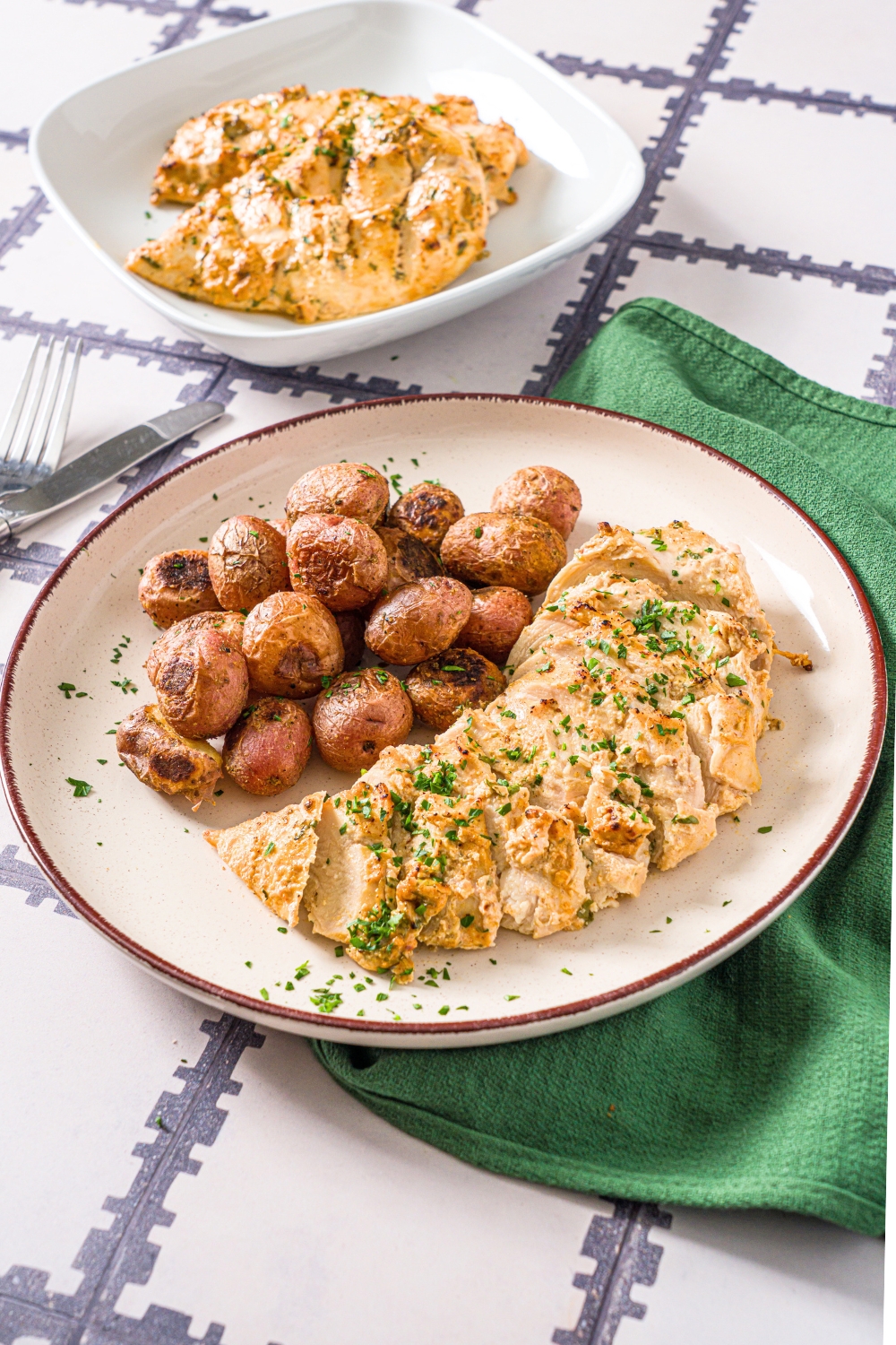 Greek yogurt marinated chicken breast sliced on a white plate with baby potatoes.