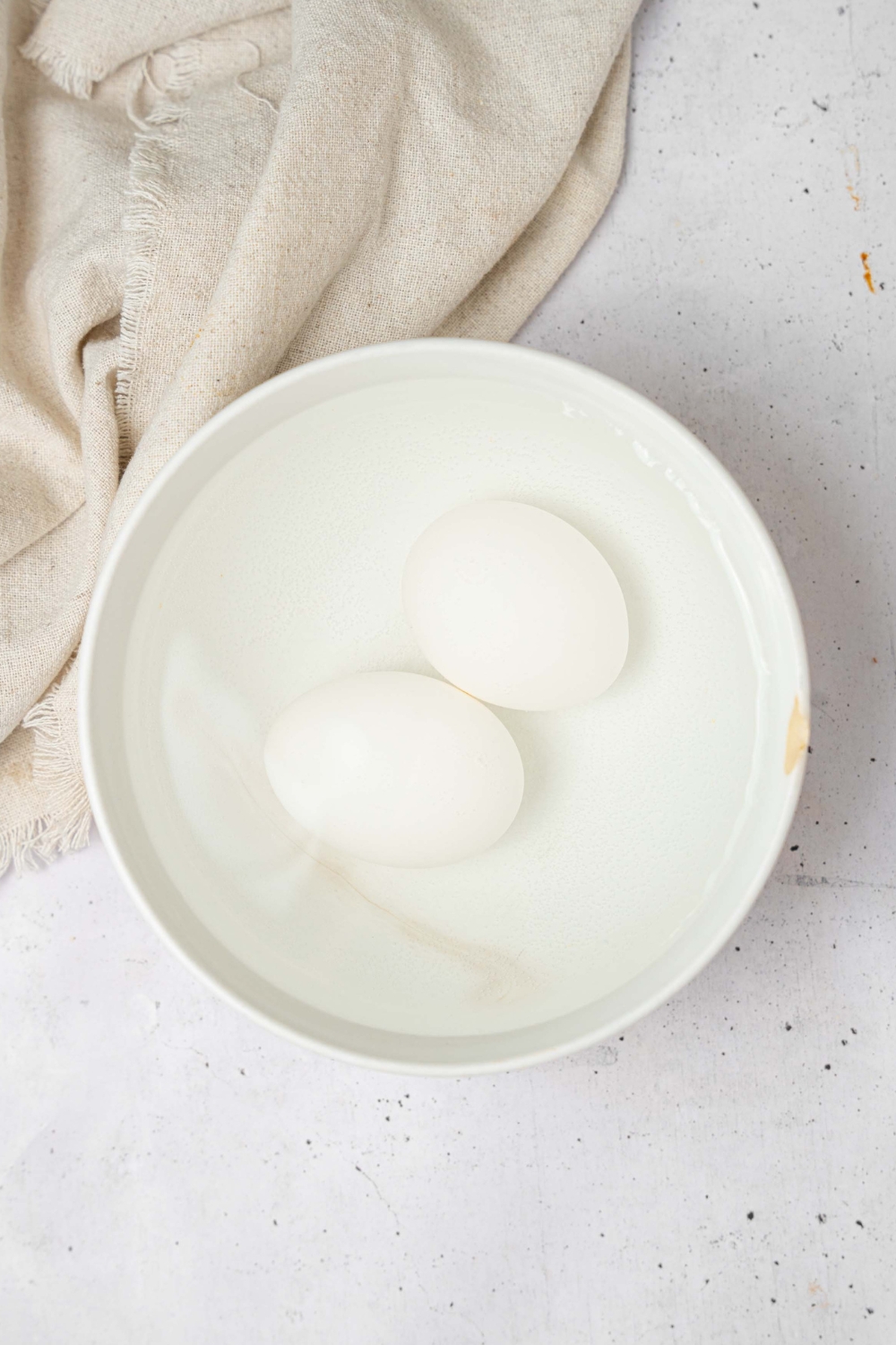 Two eggs in a white bowl of water.