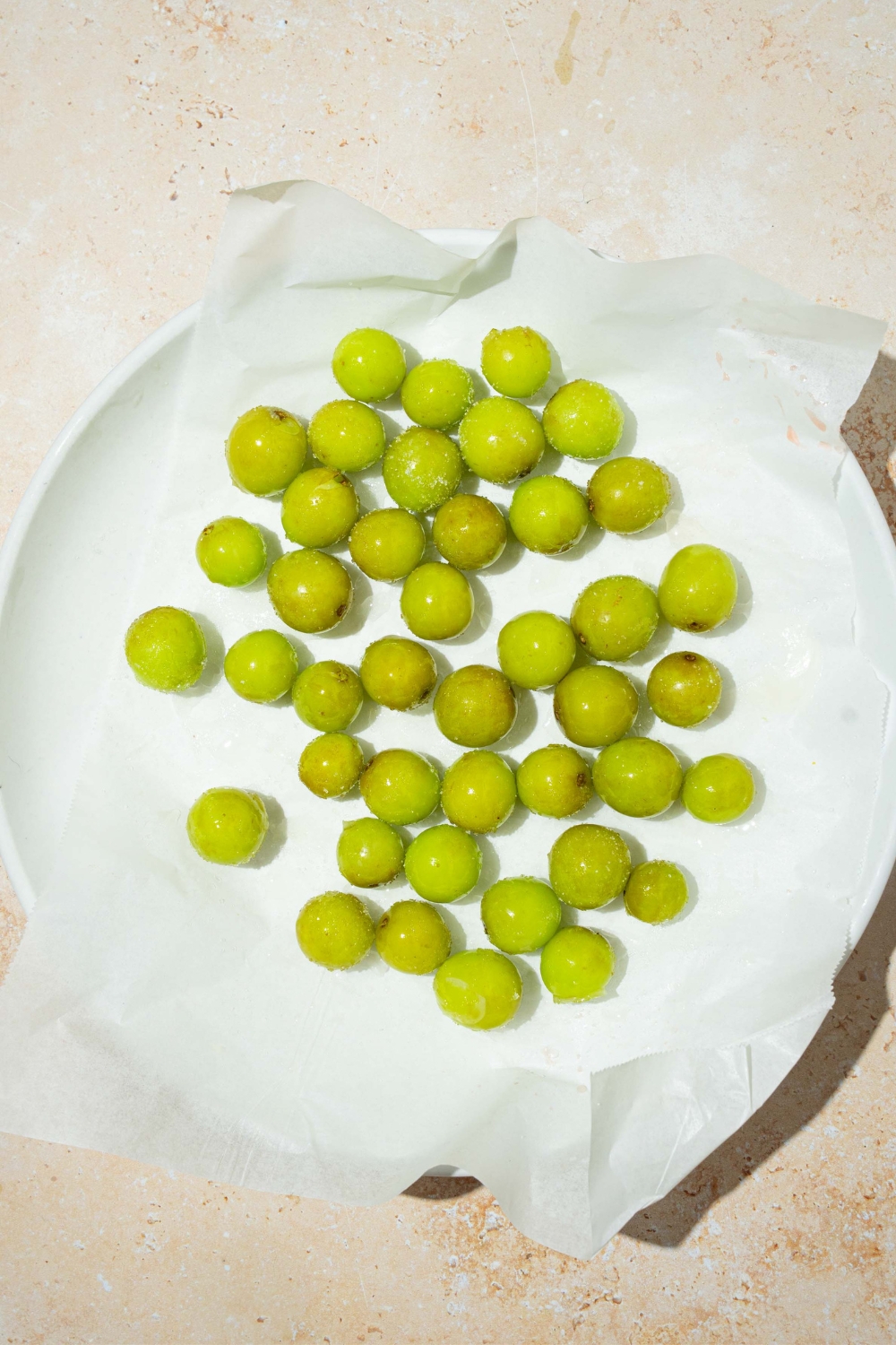 A bunch of frozen sour patch grapes on paper towels on top of a white plate.