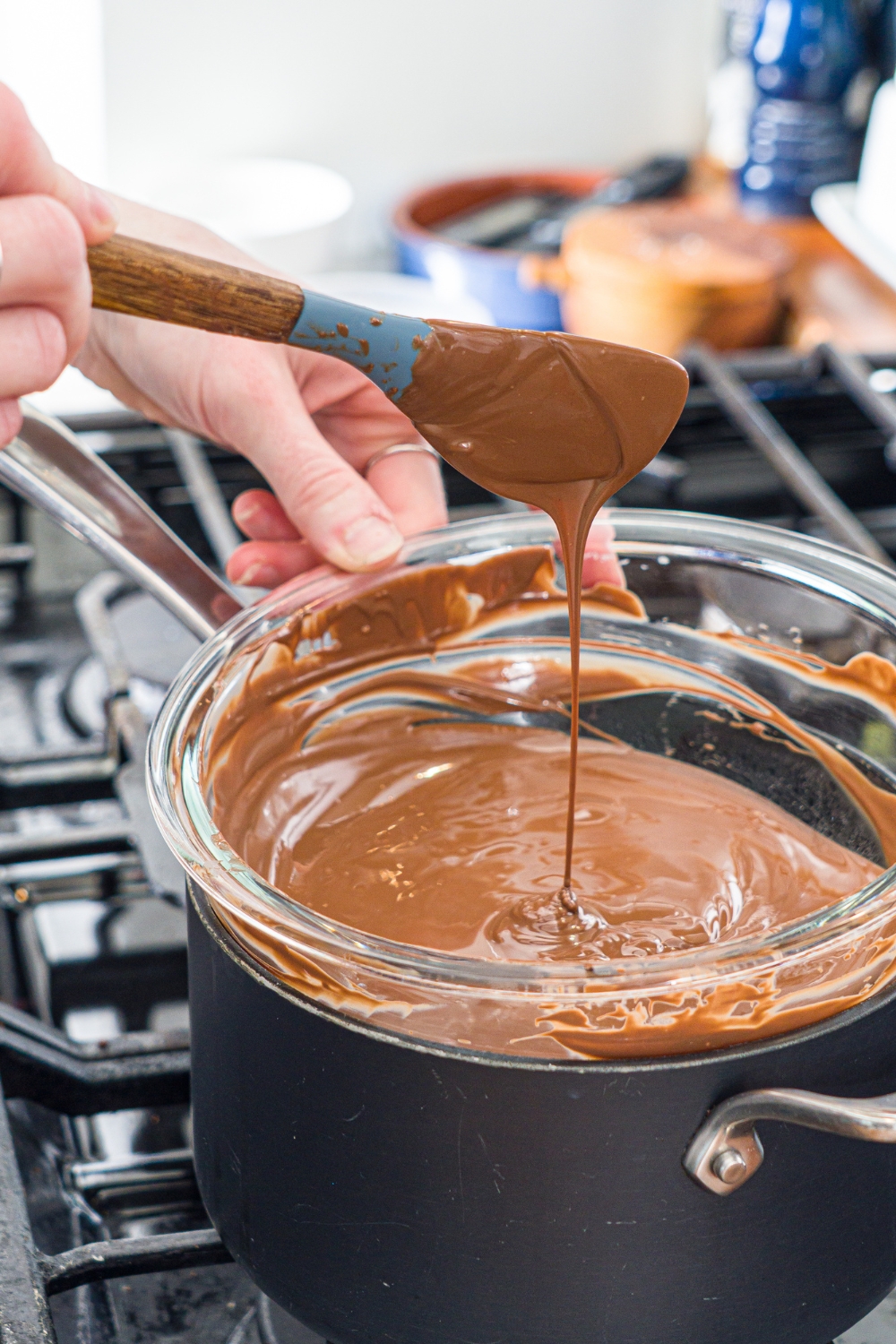 A rubber spatula with chocolate on it being drizzled into a glass bowl with melted chocolate in it on top of a black pot.