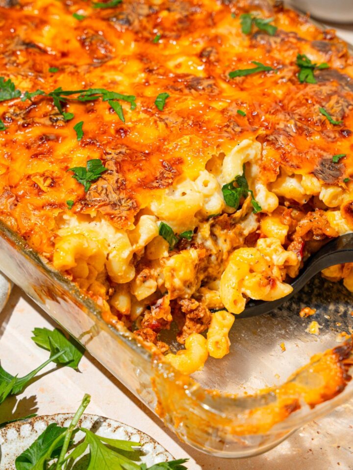 Part of a glass baking dish with mac & cheese lasagna in it. Part of the mac & cheese lasagna is missing from the front of it.