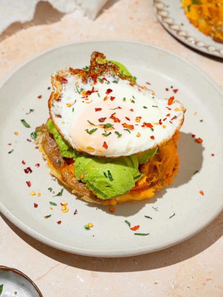A sunny side up egg on top of smashed avocado on top of a potato waffle.