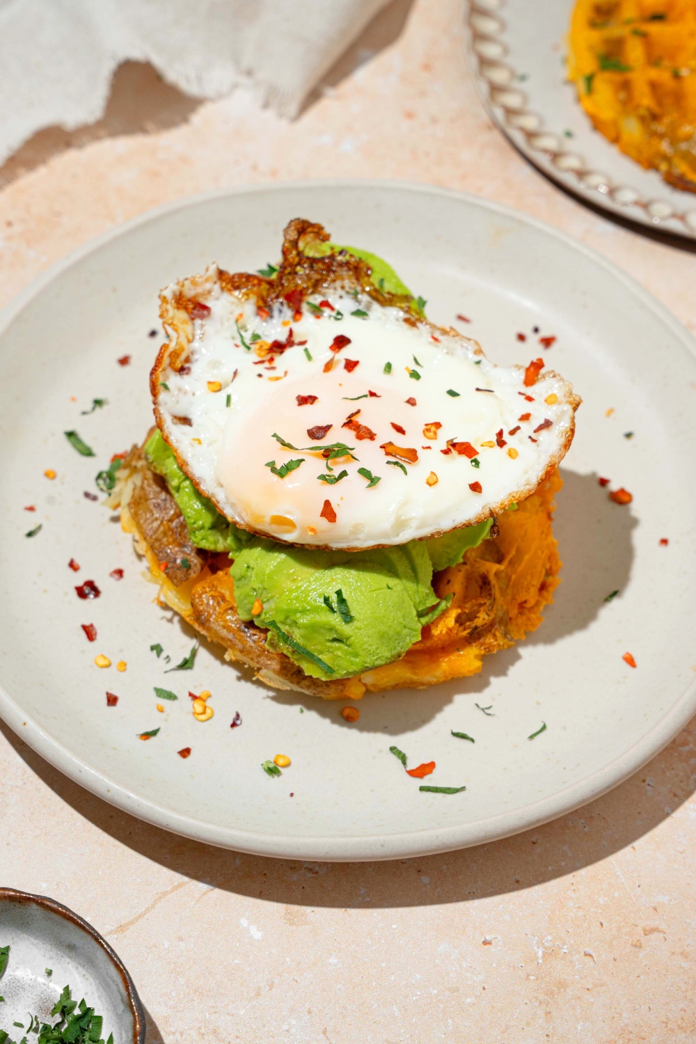 A sunny side up egg on top of smashed avocado on top of a potato waffle.