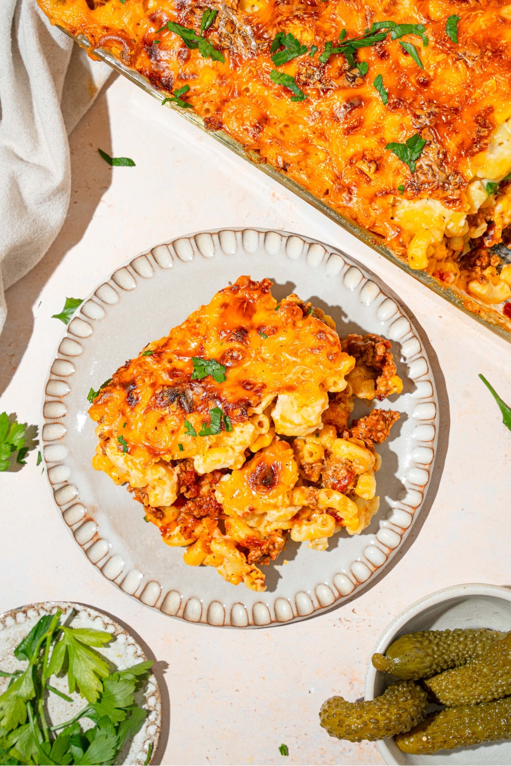 Mac & cheese lasagna on top of a white plate with the baking dish with the mac & cheese lasagna behind it.