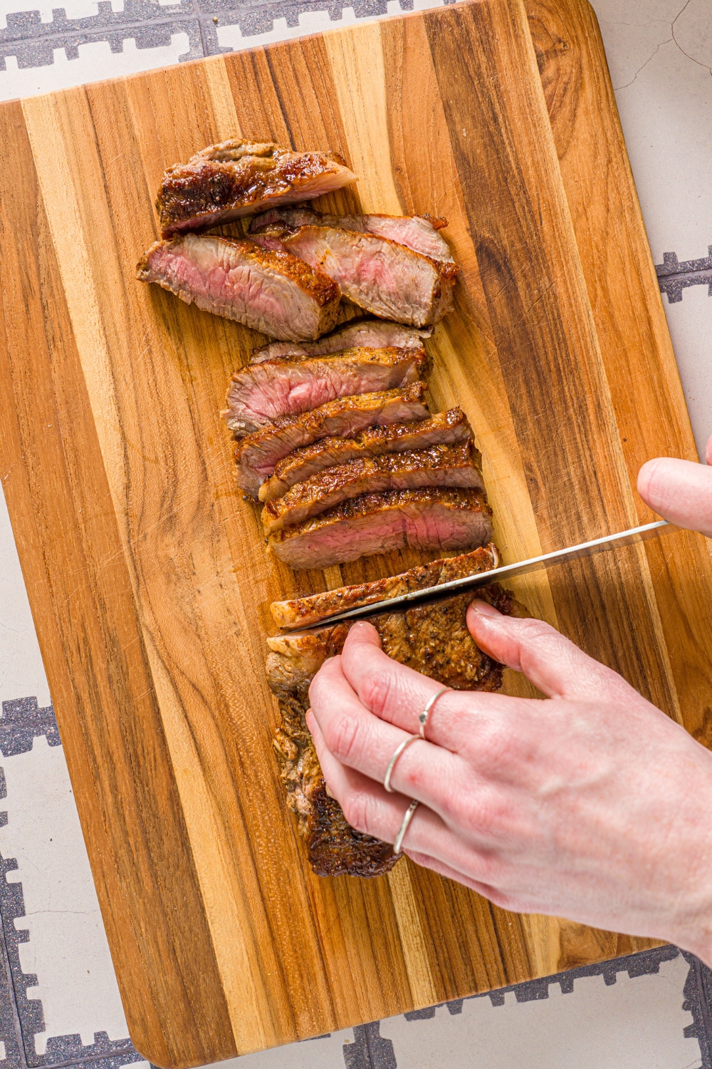 A hand holding a knife slicing a new york strip steak on a wooden cutting board for a cajun steak pasta.