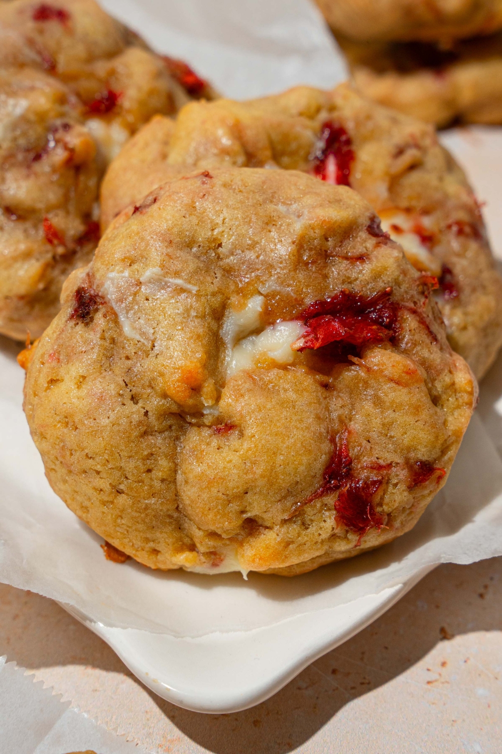 A white plate lined with parchment paper with several strawberry cheesecake cookies. The plate is on a tan counter.