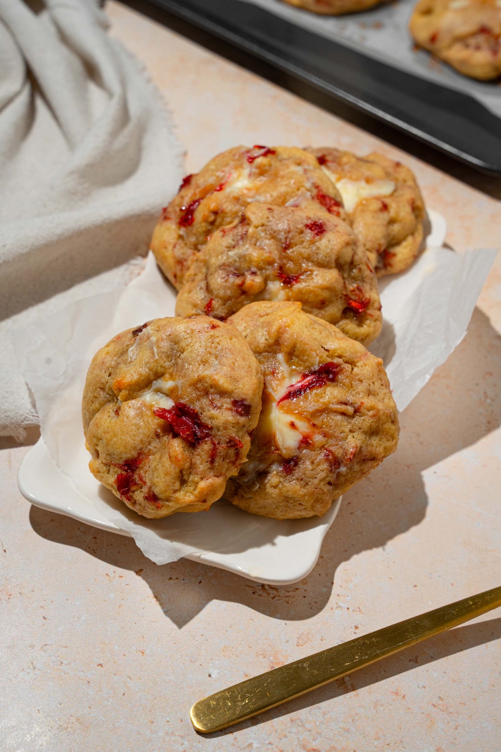 A white plate lined with parchment paper with several strawberry cheesecake cookies. The plate is on a tan counter.