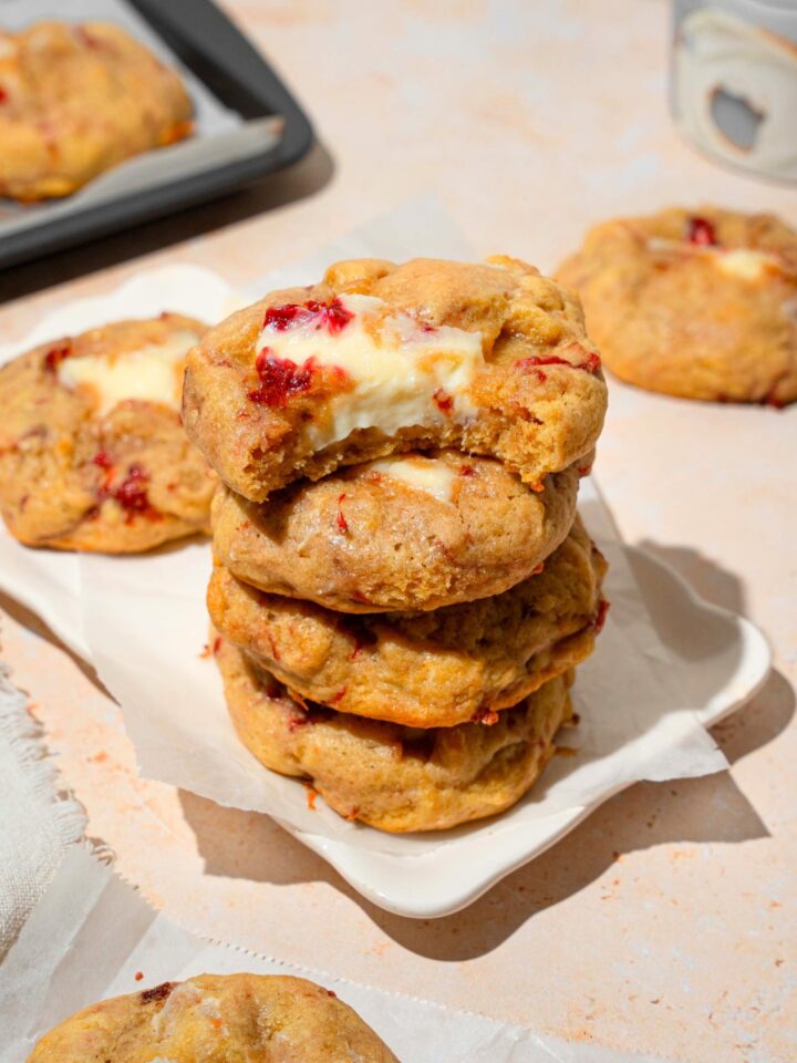 Four strawberry cream cheese cookies stacked on top of one another. The top cookie has a bite out of the front of it.