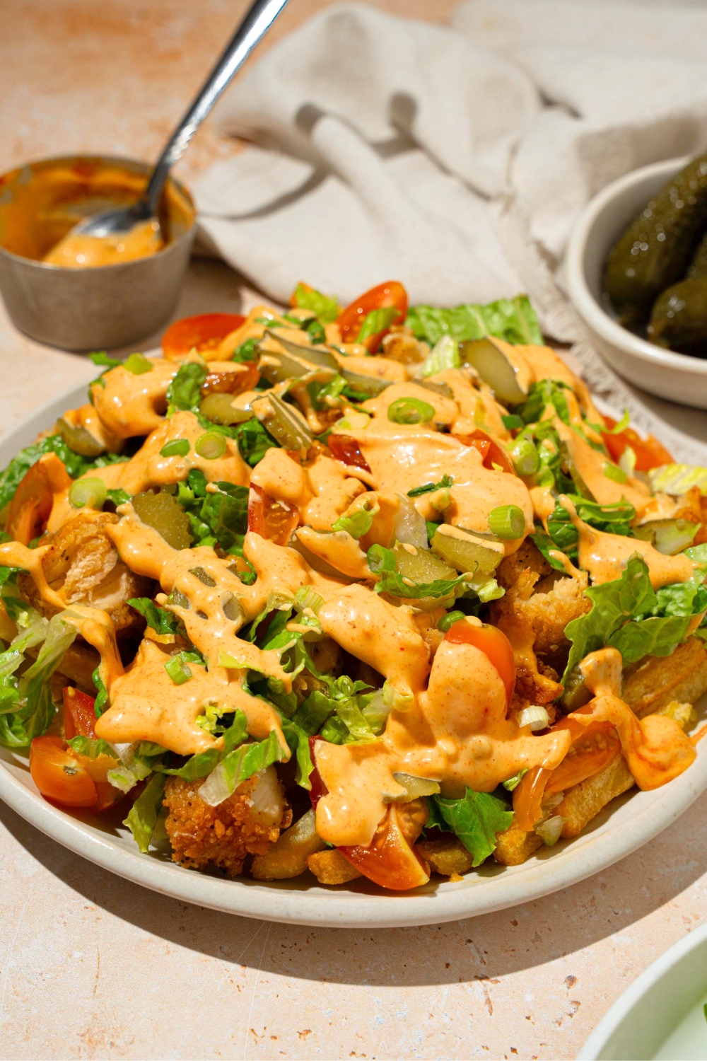 Chicken burger bowl loaded fries on a white plate with crispy chicken, french fries, lettuce, tomatoes, melted cheese, and a burger sauce on top.