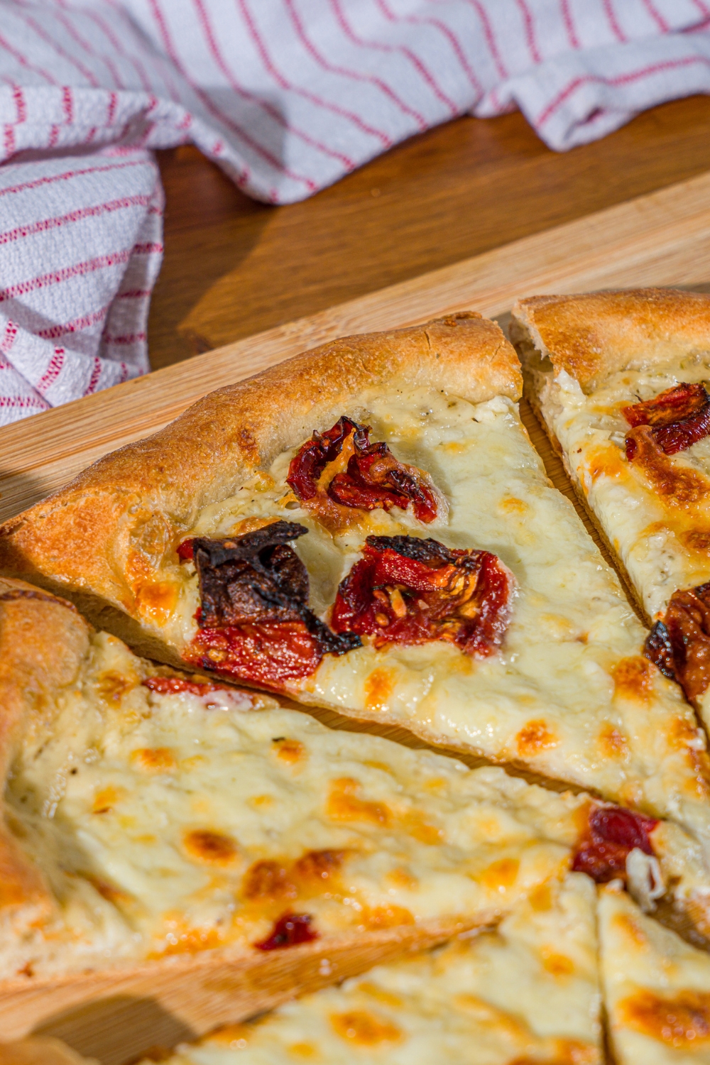 A wooden board with a sliced garlic white pizza topped with roasted peppers. The board is on a wooden counter.