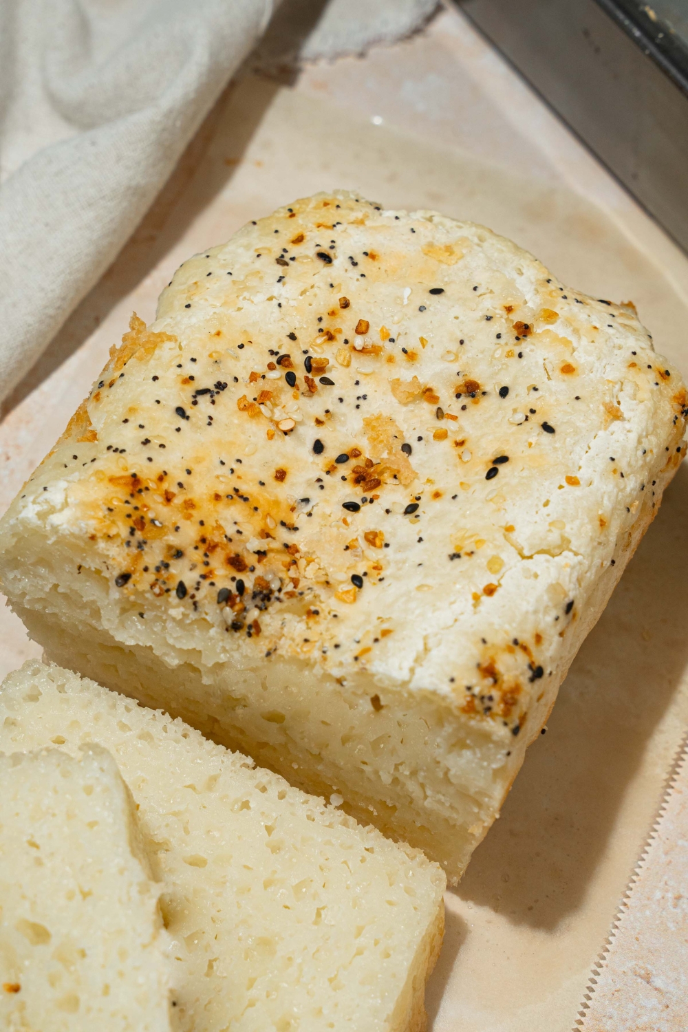 A loaf of sliced blender rice bread topped with everything bagel seeds. The loaf is on a piece of parchment paper on a tan counter.