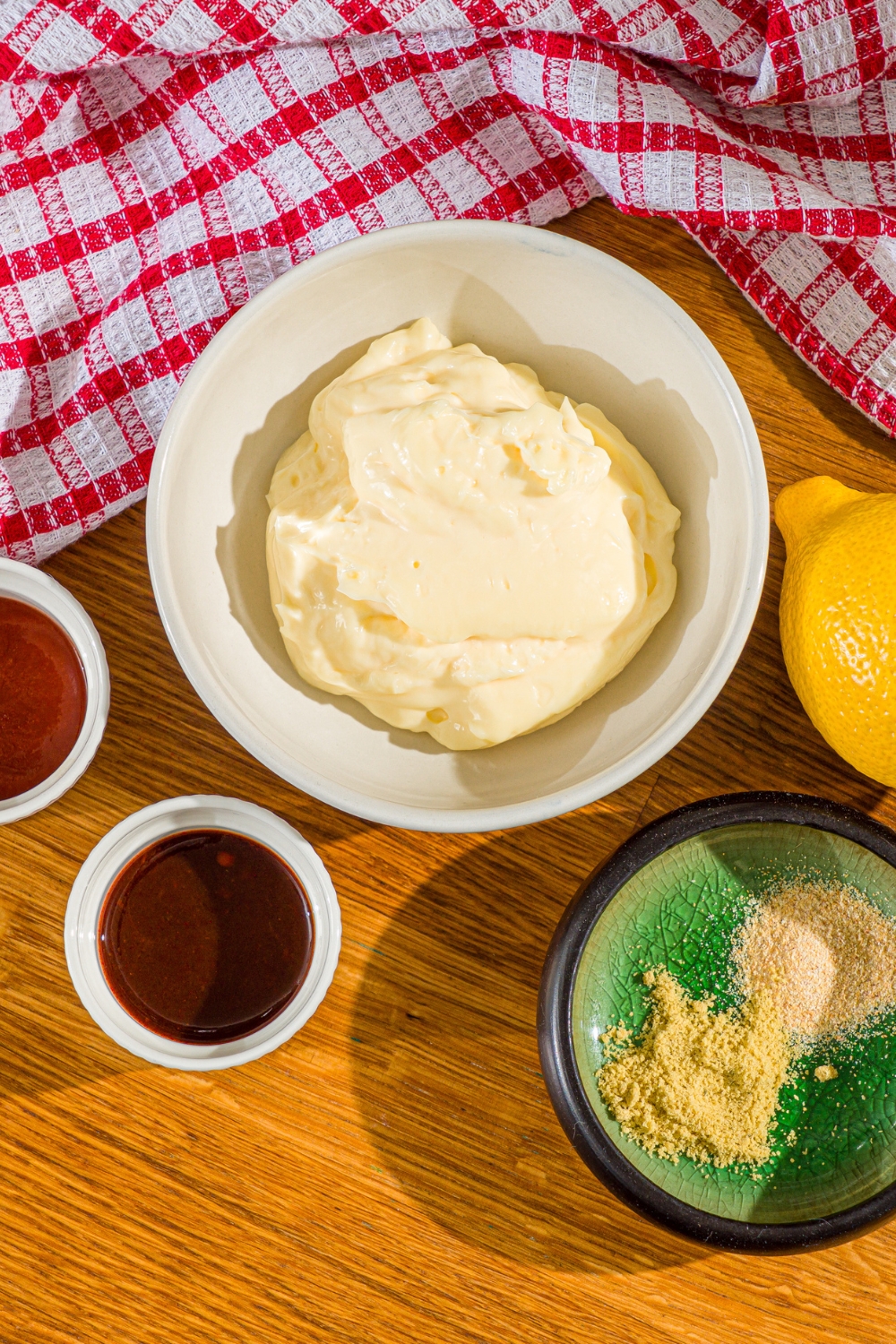 A wooden counter with bowls of ingredients to make comeback sauce including mayo, sriracha, chipotle sauce, lemon, and seasonings.