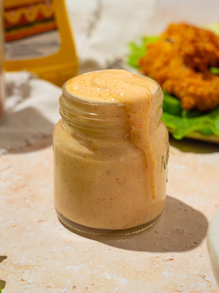 A jar of Burger King zesty sauce on a tan counter with a plate of chicken strips with lettuce.