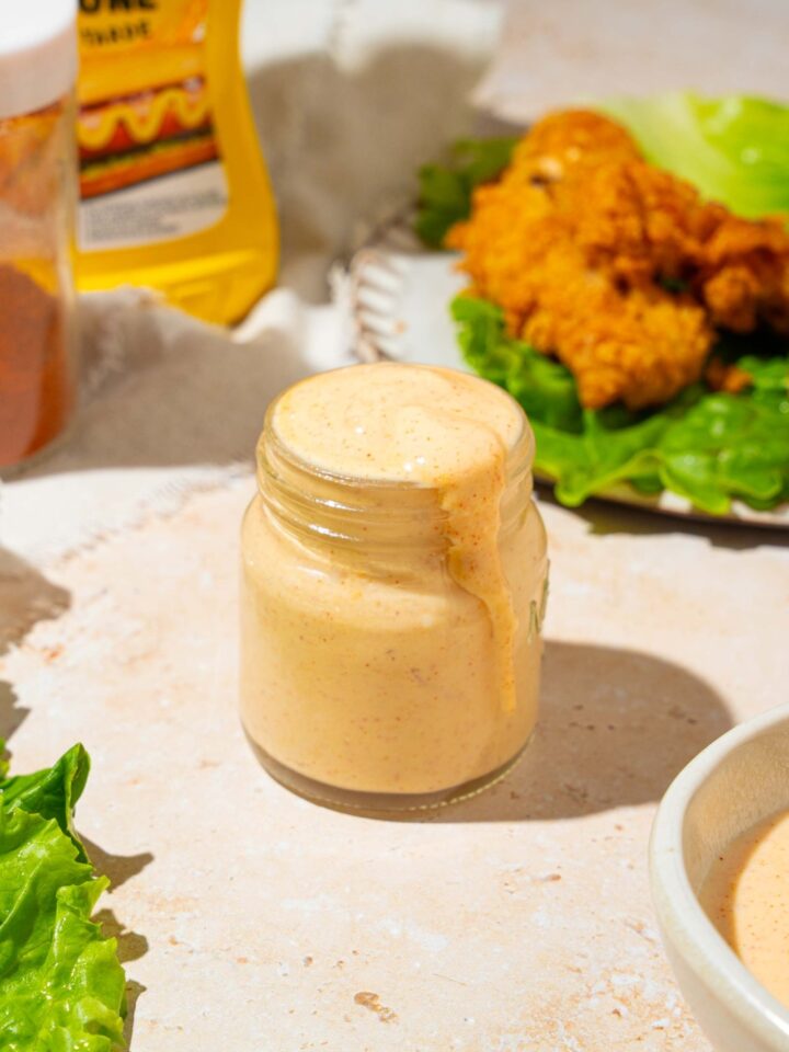 A jar of Burger King zesty sauce on a tan counter with a plate of chicken strips with lettuce, and an additional bowl of sauce.