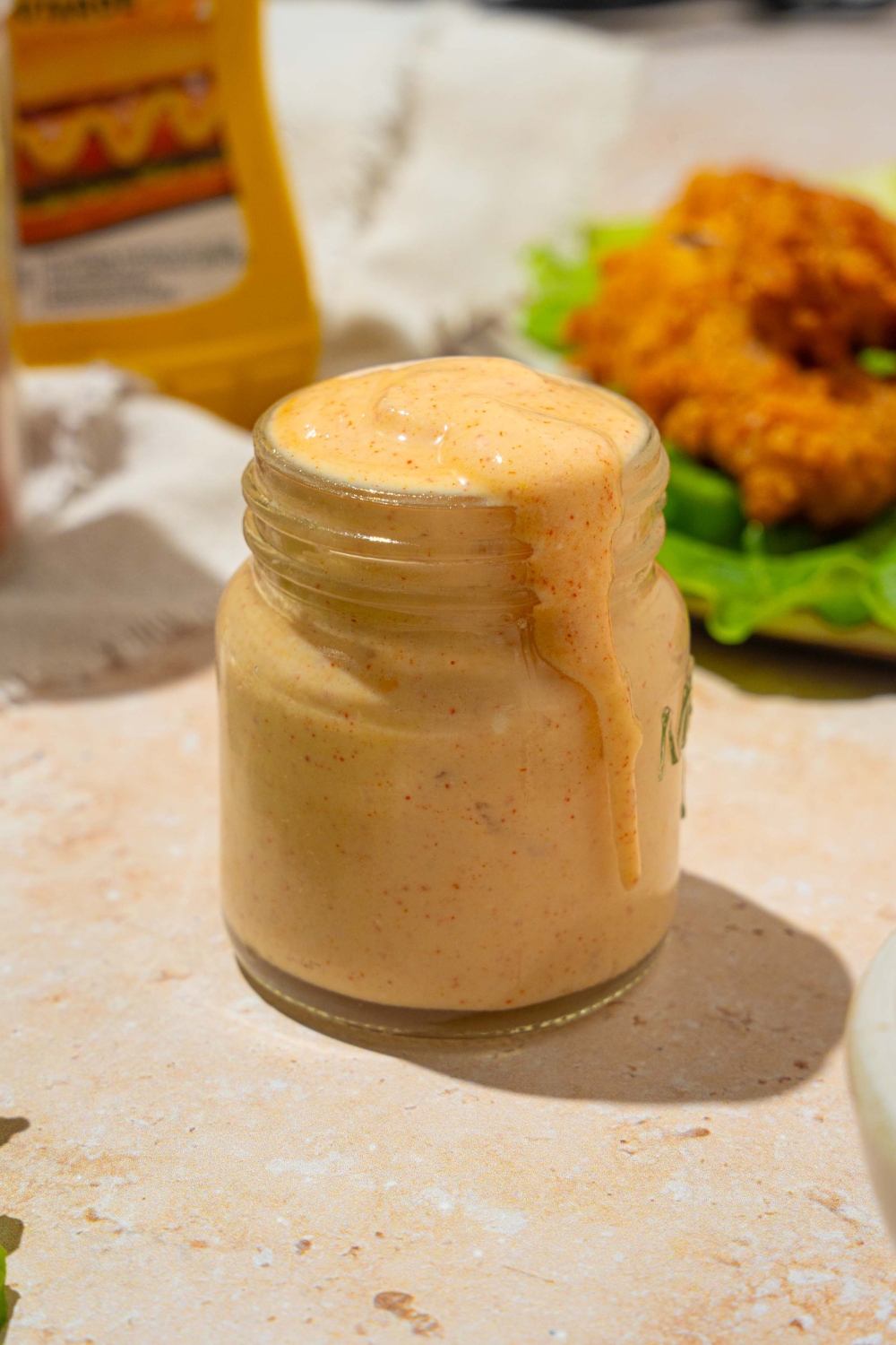 A jar of Burger King zesty sauce on a tan counter with a plate of chicken strips with lettuce.