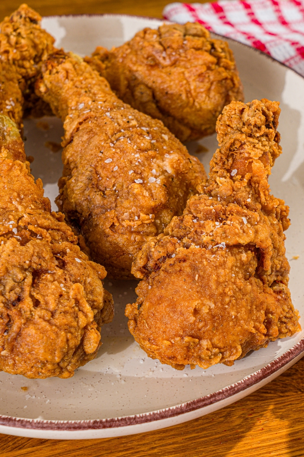 A white plate with copycat KFC original chicken recipe. The plate is on a wooden counter with a red checkered napkin.