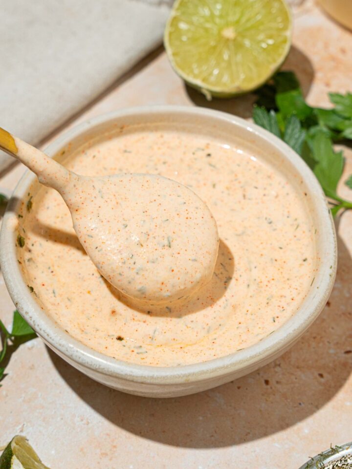 A white bowl with Popeyes blackened ranch. A spoon is dipped in the bowl. The bowl is on at tan counter with a lime.