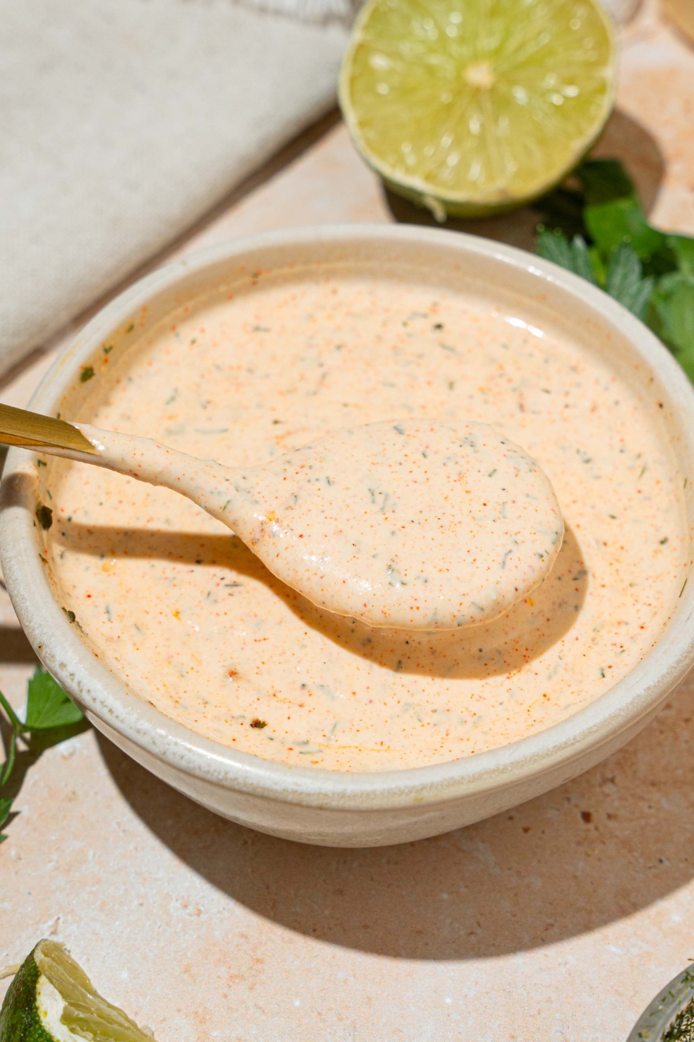 A white bowl with Popeyes blackened ranch. A spoon is dipped in the bowl. The bowl is on at tan counter with a lime.