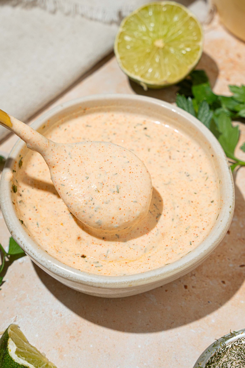 A white bowl with Popeyes blackened ranch. A spoon is dipped in the bowl. The bowl is on at tan counter with a lime.