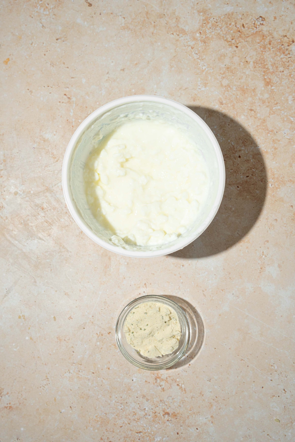 A tan counter with a bowl of cottage cheese and a bowl of ranch seasoning.