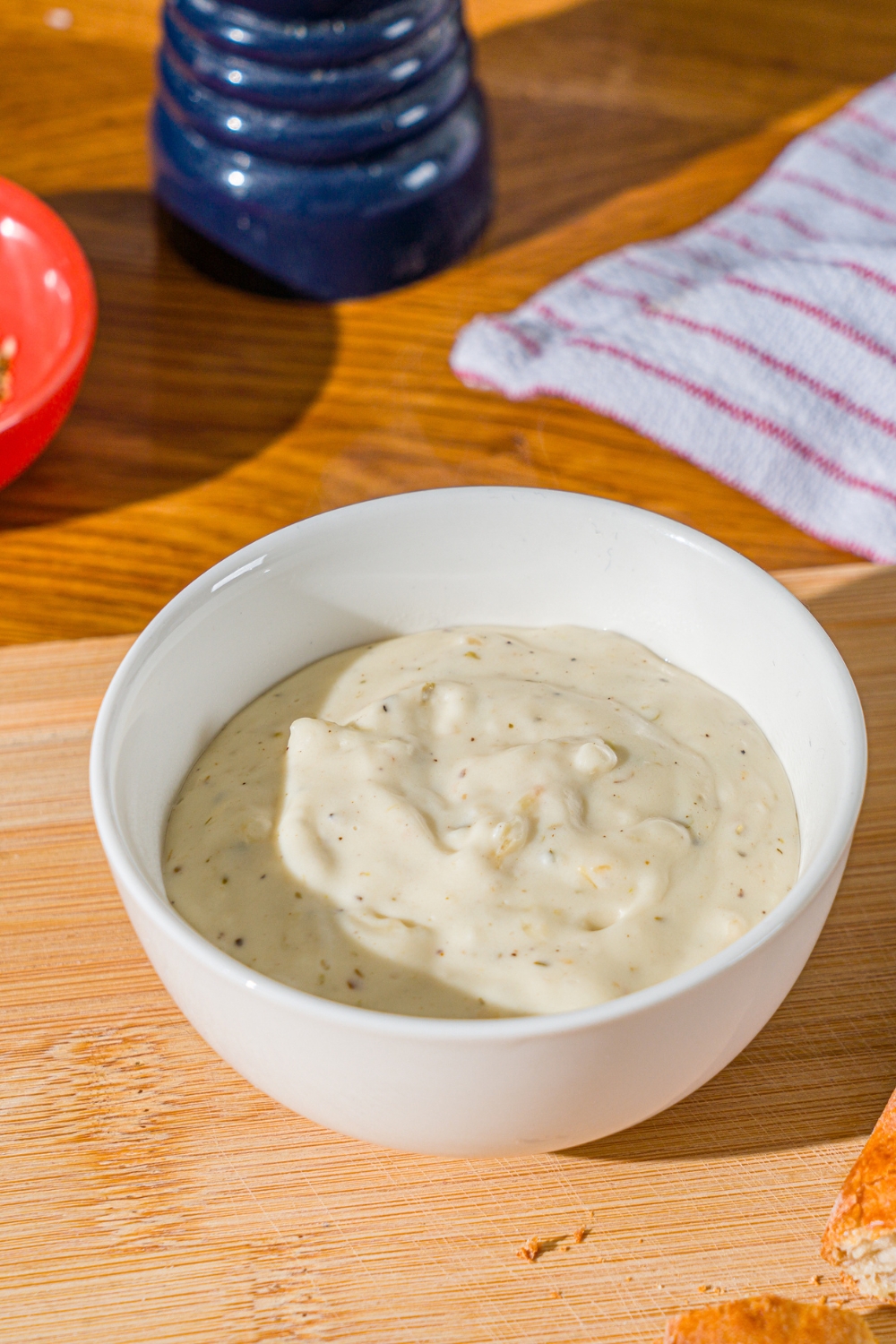 A white bowl with garlic white pizza sauce. The bowl is on a wooden counter with a white striped napkin.