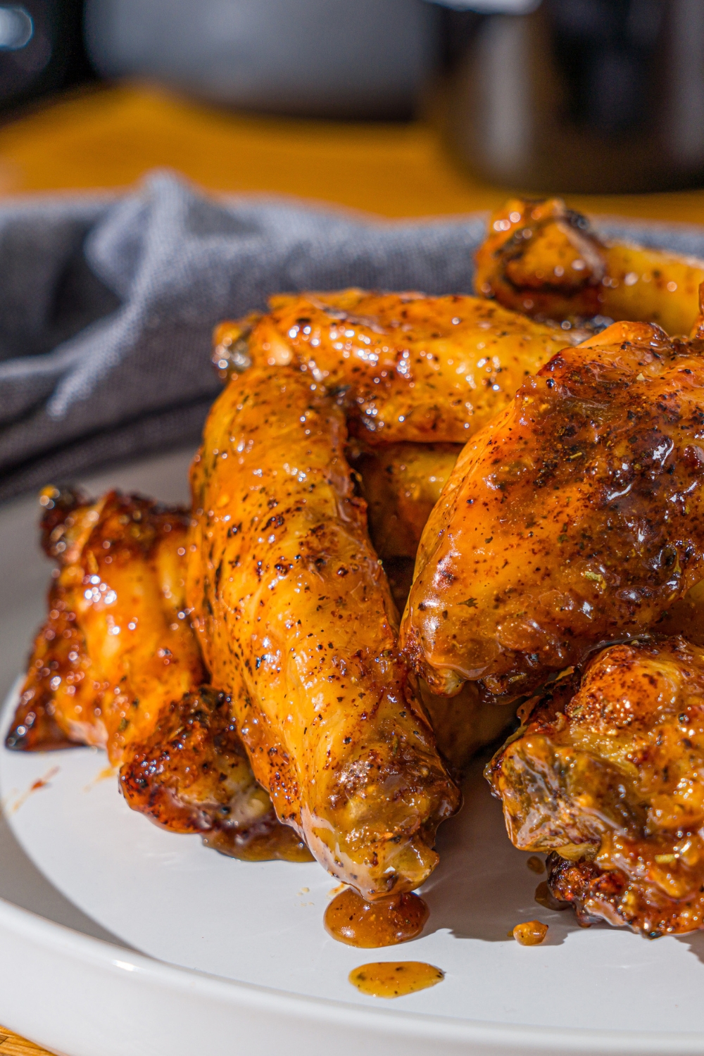 A white plate with a pile of crispy honey lemon pepper wings. The plate is on a wooden counter with a blue cloth napkin.