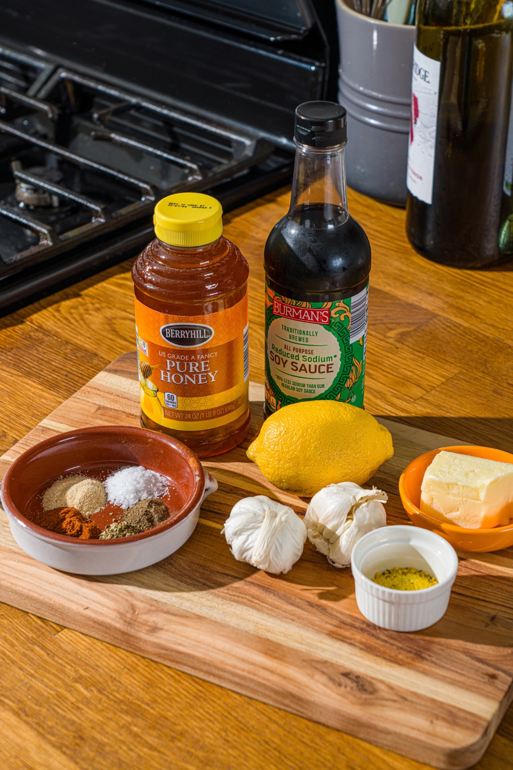 A wooden board with ingredients to make crispy honey lemon pepper wings including honey, soy sauce, lemon, garlic, butter, oil, and seasonings.