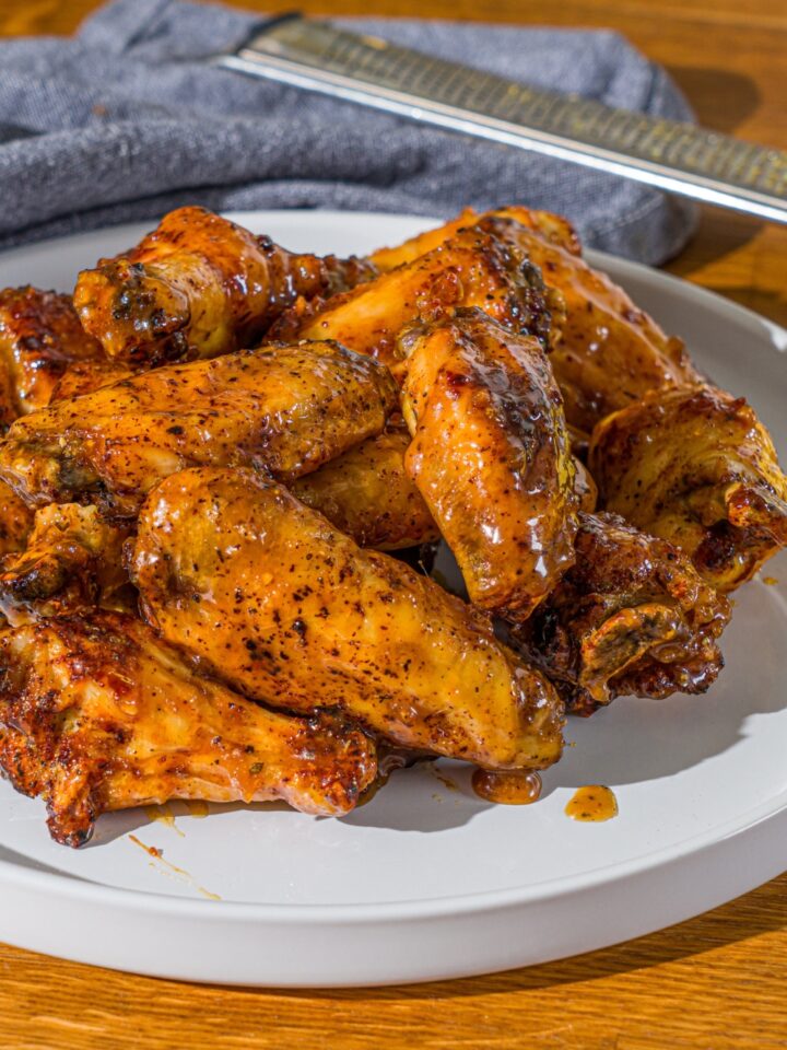 A white plate with a pile of crispy honey lemon pepper wings. The plate is on a wooden counter with a blue cloth napkin.