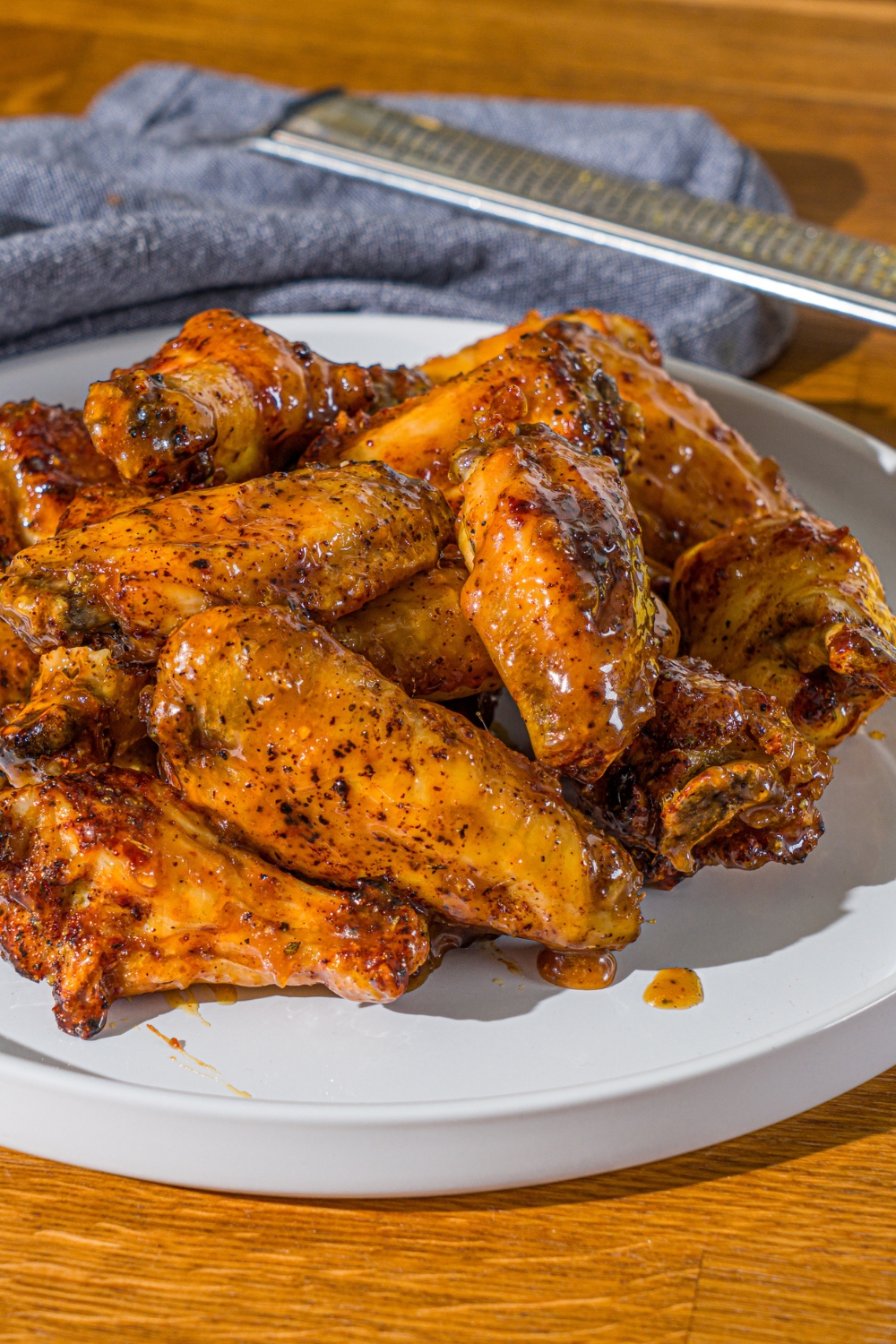 A white plate with a pile of crispy honey lemon pepper wings. The plate is on a wooden counter with a blue cloth napkin.