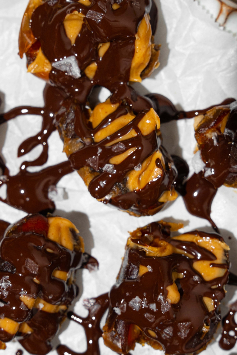 A plate lined with parchment paper with dates stuffed with peanut butter and drizzled with chocolate and sea salt.